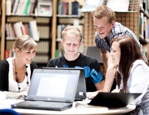 Group of smiling young adults around a laptop in a library