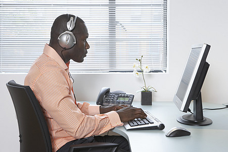 Young man using computer at desk, wearing headphones