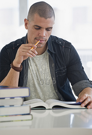 Young man chewing pencil while studying