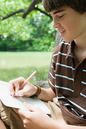 Boy writing on paper on the grass