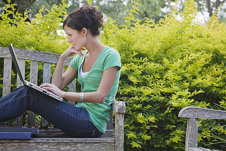 Young woman using laptop on park bench
