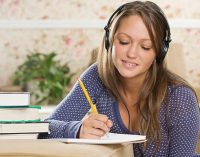 Young woman wearing headphones and doing homework