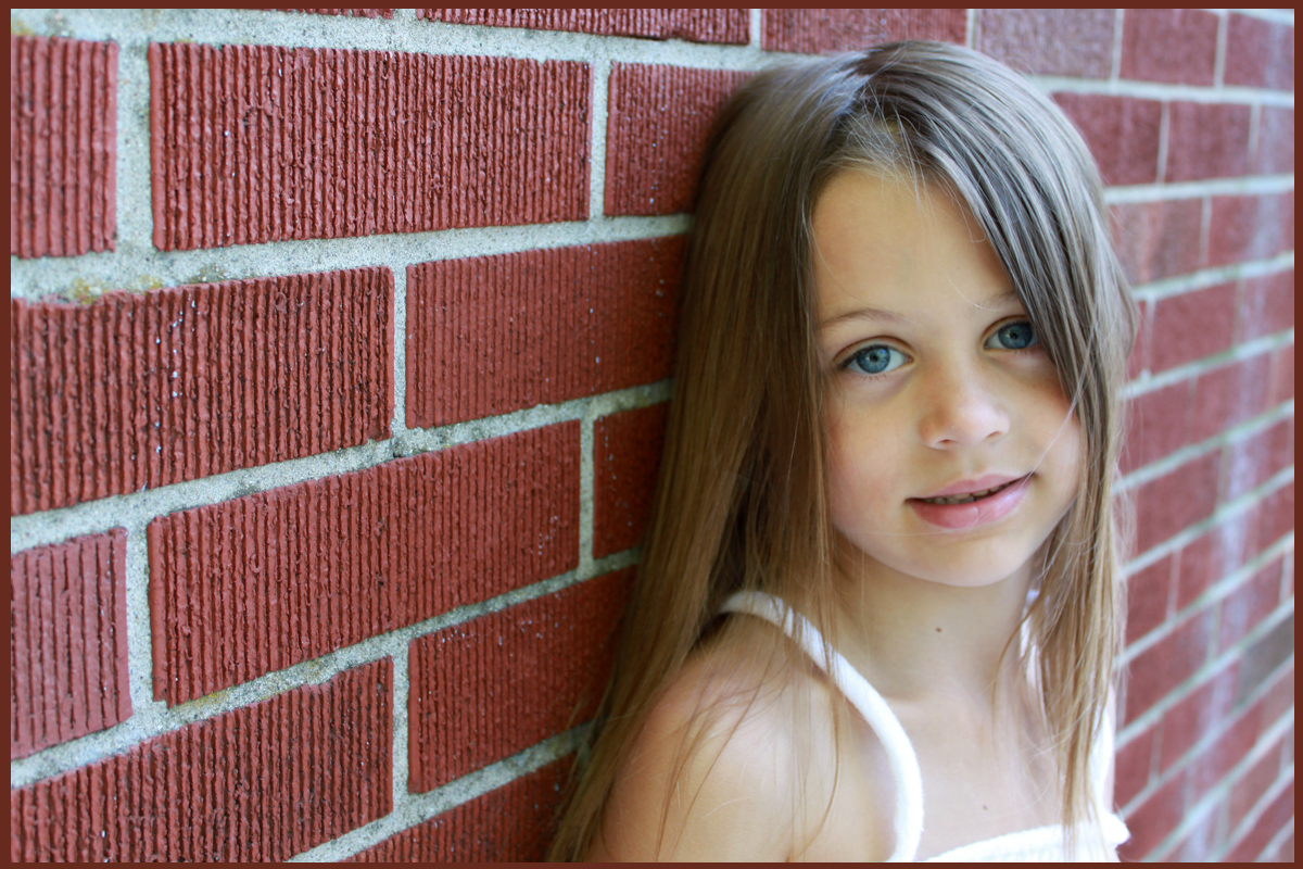 Young girl leaning against brick wall